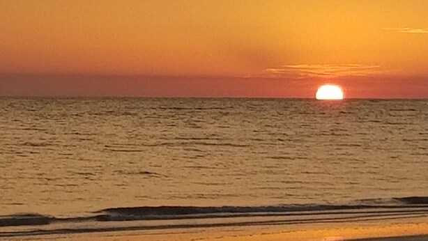 Solnedgang over havet med rolige bølger og en klar horisont.
