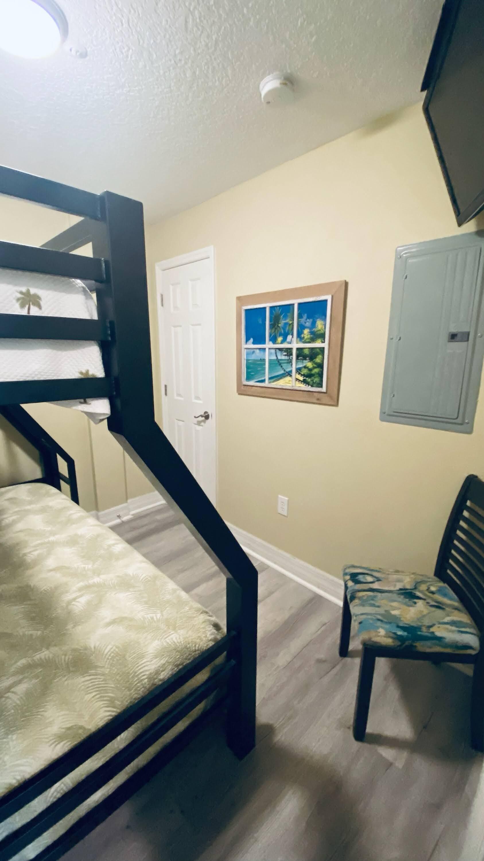 A room with a bunk bed, a chair, a door, and a framed picture on the wall.