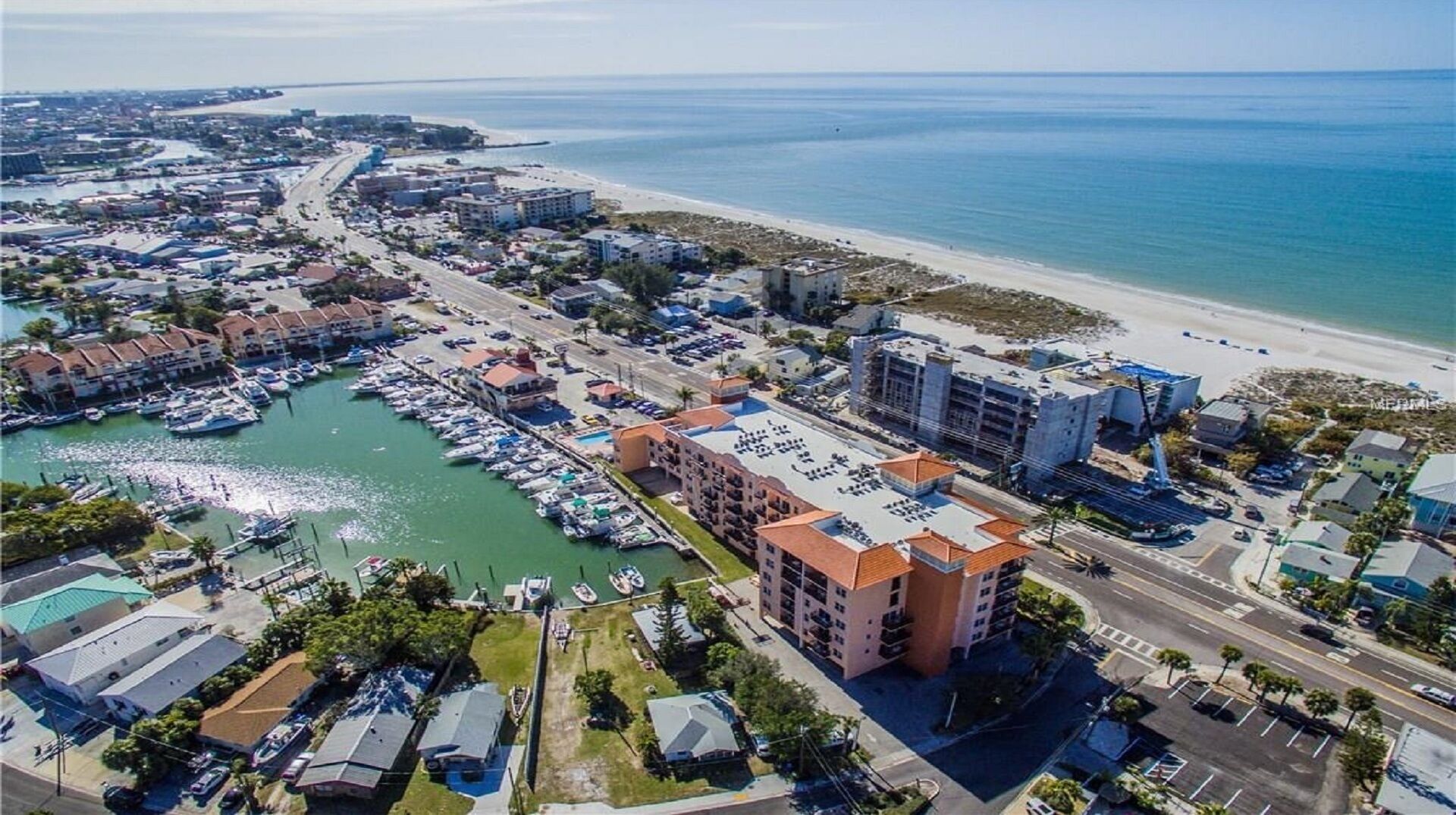 Un pueblo costero con puerto deportivo, playa y una combinación de edificios residenciales y comerciales.