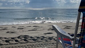 Une plage avec un ciel dégagé, un soleil brillant, et une chaise et un seau sur le sable.