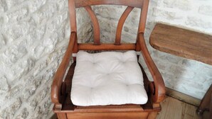 Une chaise en bois dotée d’un siège et d’un dossier rembourrés, placée contre un mur en pierre à la texture particulière.