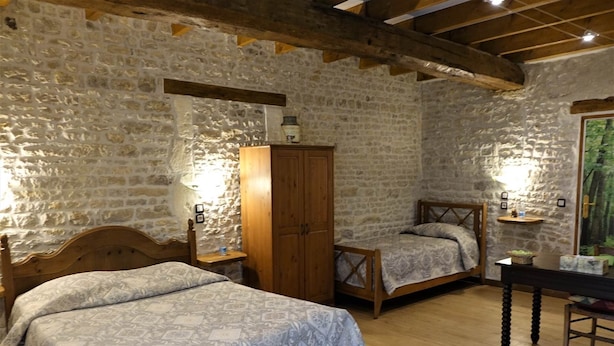 Une chambre avec deux lits, des meubles en bois, des murs en pierre et un plafond en bois.