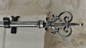 Une tringle à rideaux en métal, ornée d’un embout décoratif et fixée à un support simple, le tout placé devant un mur à texture.