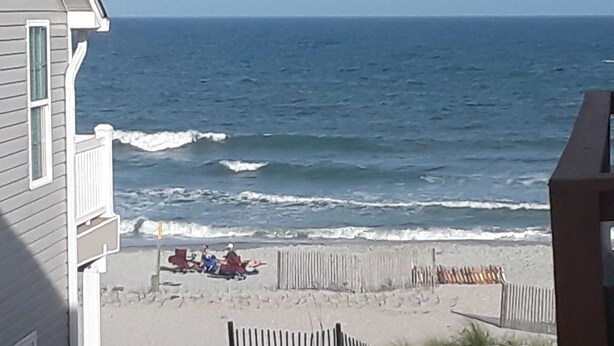 Een uitzicht op het strand met een houten omheining en een huis op de voorgrond.