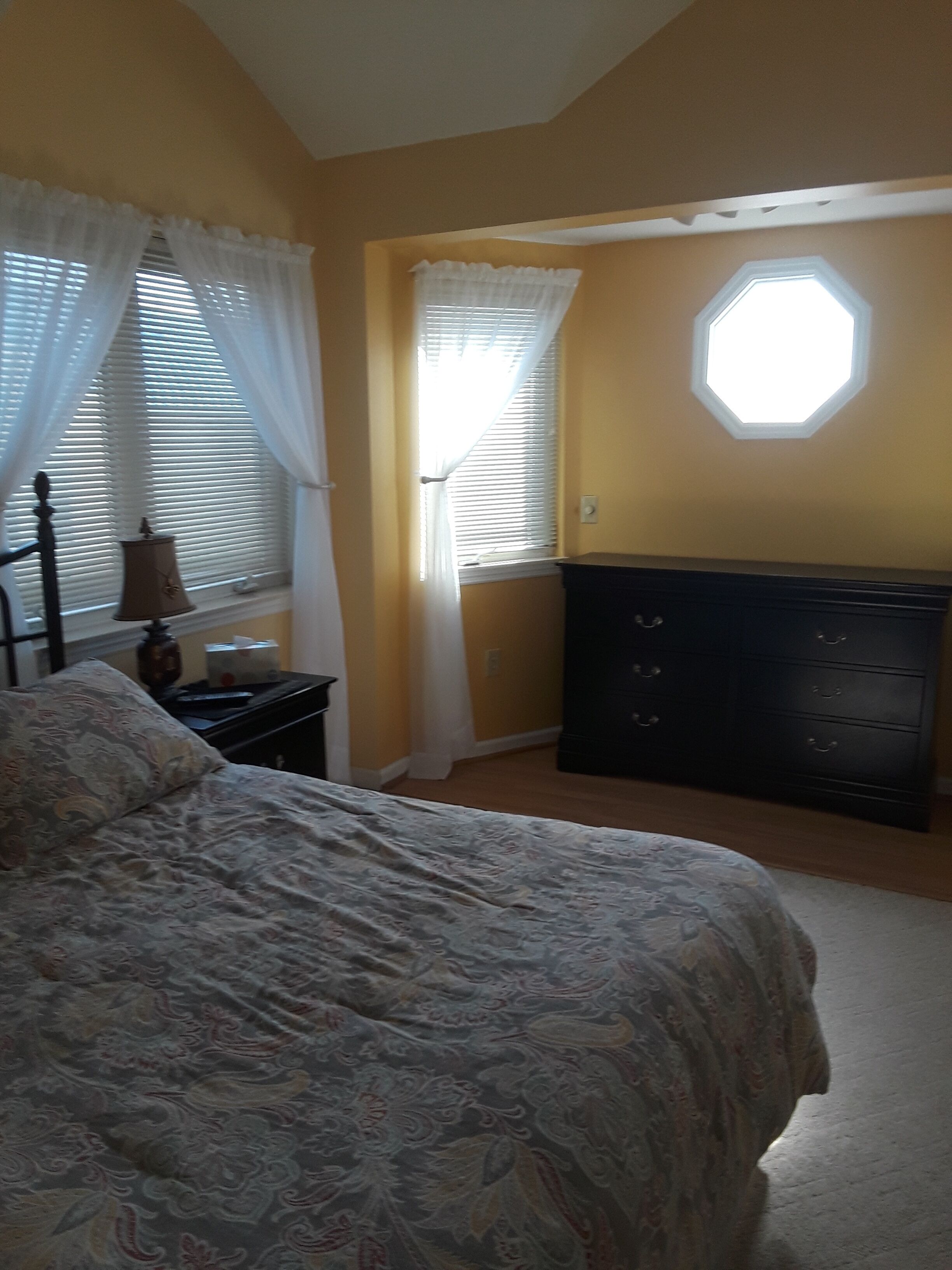 Ein Schlafzimmer mit Bett, Kommode und einem Fenster mit Jalousien.