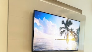 A flat-screen TV mounted on a wall with a wooden shelf below. - Luquillo Beach Getaway – Cozy Coastal Condo Steps from  Playa Azul (Luquillo)