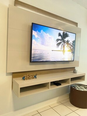 A flat-screen TV mounted on a wall with a wooden shelf below. - Luquillo Beach Getaway – Cozy Coastal Condo Steps from  Playa Azul (Luquillo)