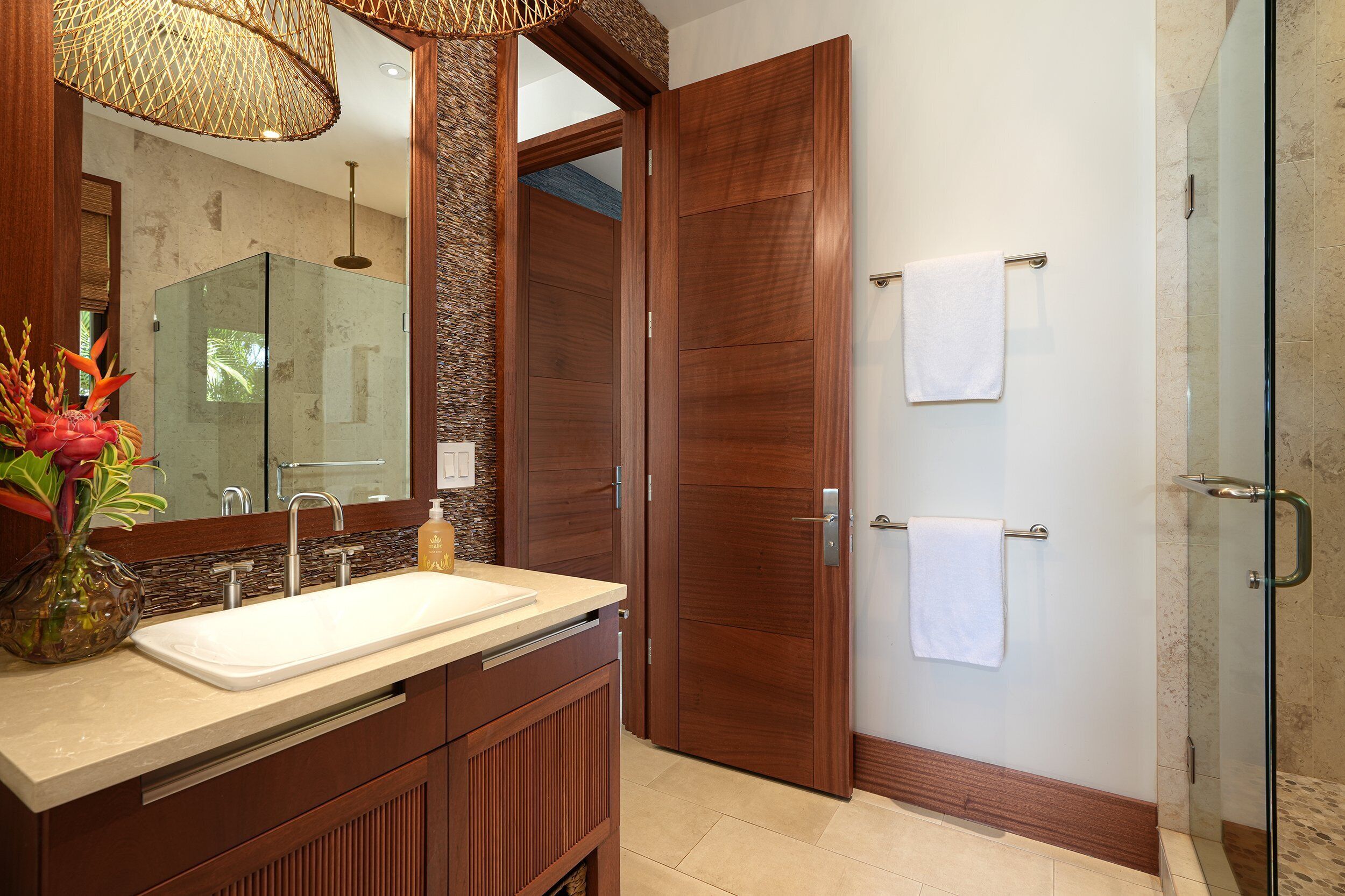 Un baño moderno con tocador de madera, cabina de ducha de vidrio y un espejo grande.