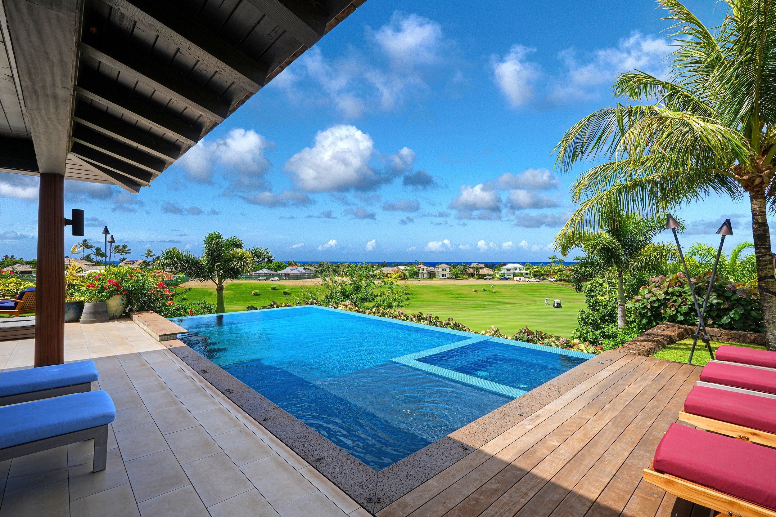 Une piscine avec une terrasse en bois, des chaises longues et une vue sur un terrain de golf.