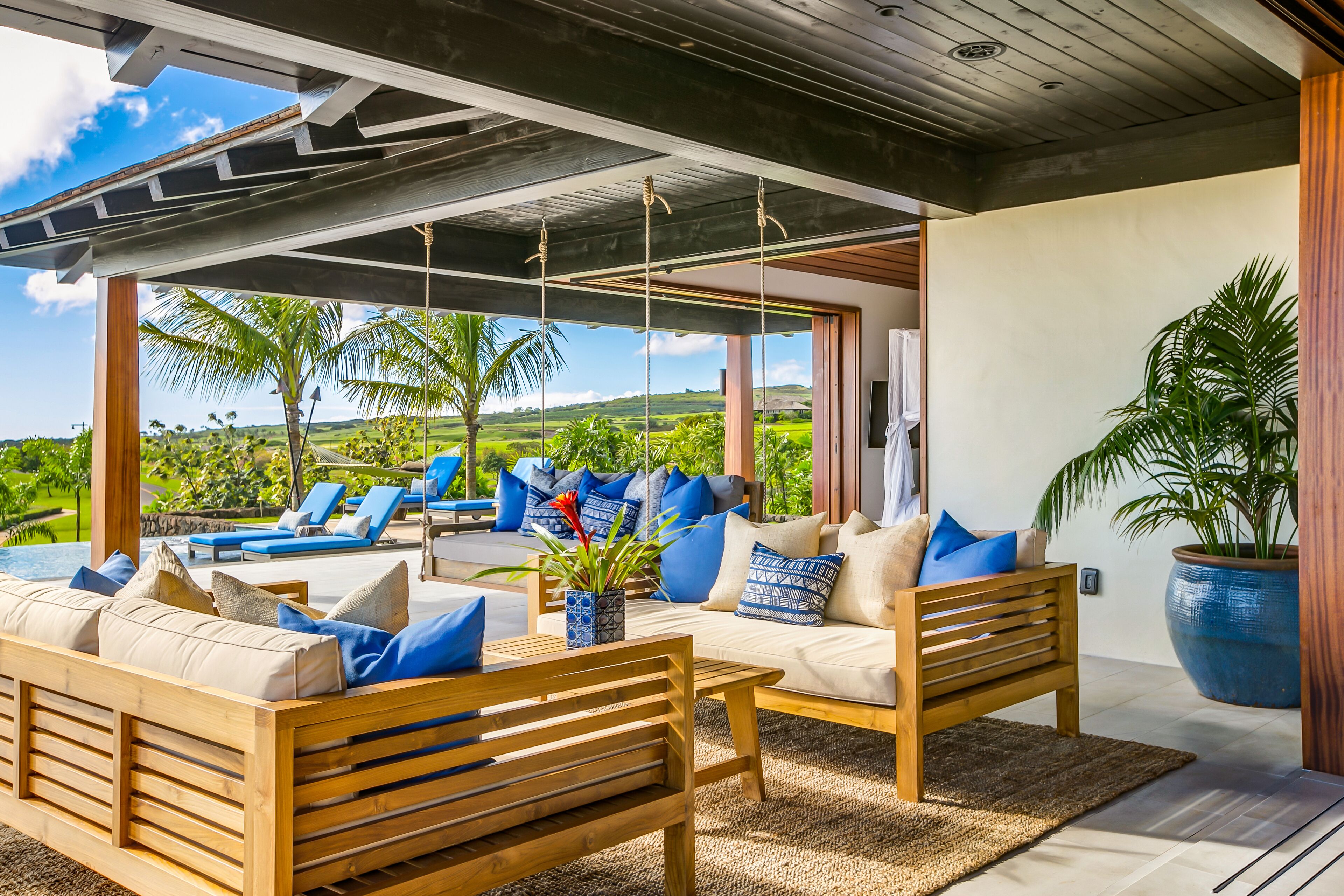 A modern outdoor seating area with wooden furniture and blue cushions, overlooking a lush landscape.