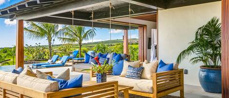 A modern outdoor seating area with wooden furniture and blue cushions, overlooking a lush landscape.