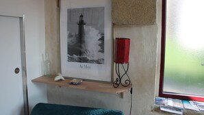 A framed photograph of a lighthouse on a shelf, a red candle holder, and a small shelf with a bottle and a tissue box. - Gouelet-Ker "Ouessant" (LOGONNA DAOULAS)