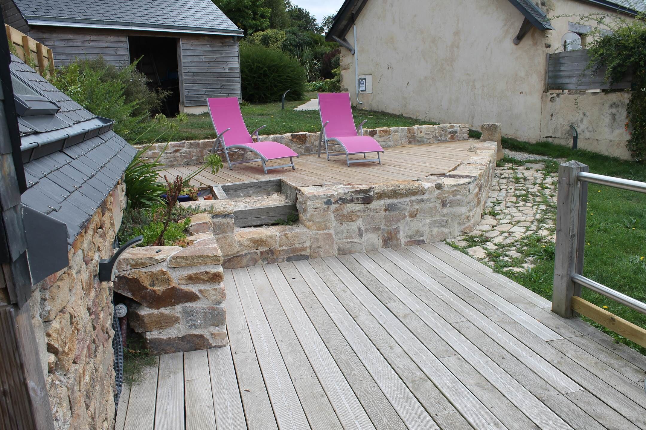 A wooden deck with two pink lounge chairs, a stone wall, and a small garden area.