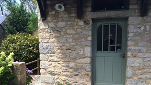 A stone building with a green door, a wooden planter with plants, and a stone wall. - "In the Land of Abers", in a valley of mills, 800m from the Aber (beaches 9 ') (Plouguin)