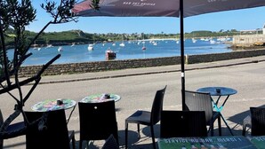 An outdoor seating area with tables and chairs, overlooking a harbor with boats. - "In the Land of Abers", in a valley of mills, 800m from the Aber (beaches 9 ') (Plouguin)