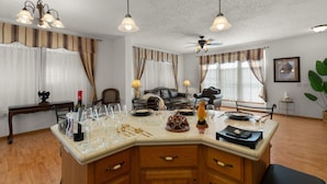 A well-lit room with a central island, a ceiling fan, and a dining area with a table set for a meal. - Yellowstone Mountain View  (Gardiner)