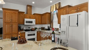 A kitchen with wooden cabinets, a white refrigerator, and a dining area set with wine glasses and cutlery. - Yellowstone Mountain View  (Gardiner)