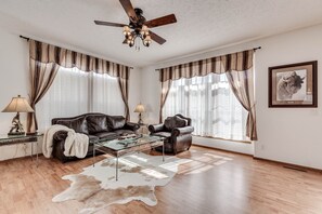 A living room with a leather sofa, a glass coffee table, and a ceiling fan.
