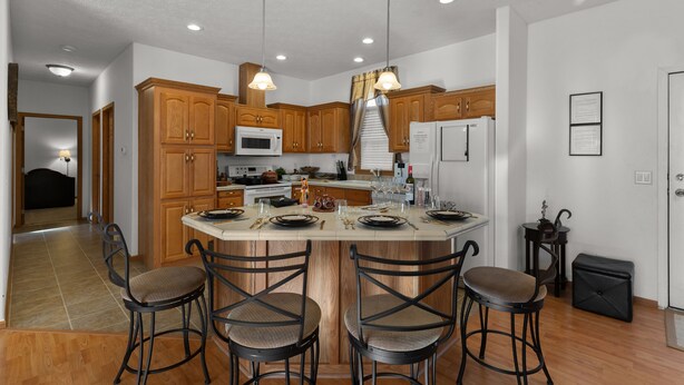 A modern kitchen with wooden cabinets, a central island with bar stools, and overhead lighting. - Yellowstone Mountain View  (Gardiner)
