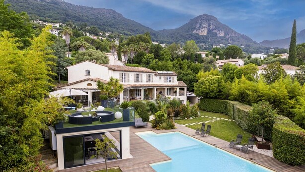 Une maison moderne avec une piscine, entourée d’une végétation luxuriante et avec des montagnes en toile de fond.