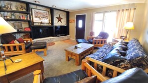 A cozy living room with a fireplace, a sofa set, a coffee table, and a bookshelf.