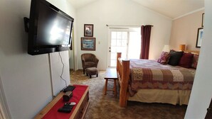 A bedroom with a bed, a chair, a TV mounted on the wall, and a window with curtains.