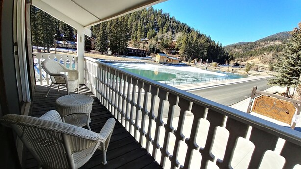 A wooden deck with wicker chairs, overlooking a swimming pool and a mountainous landscape.
