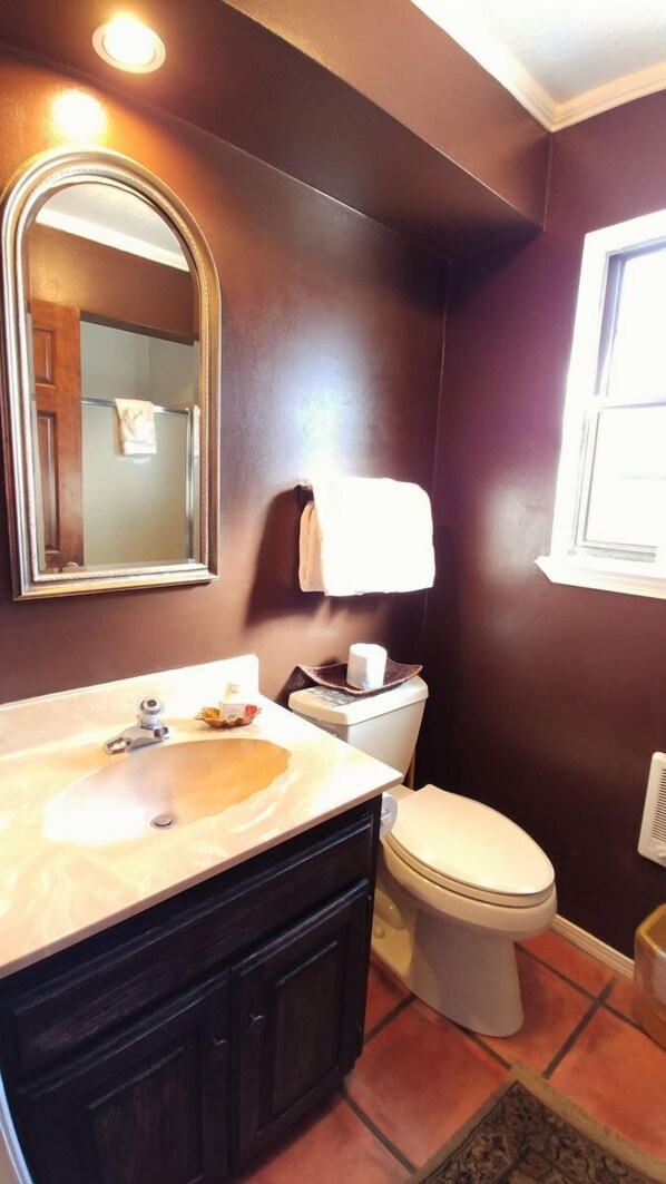 Un baño con una pared marrón oscuro, un inodoro blanco, un lavabo con espejo y una ventana.