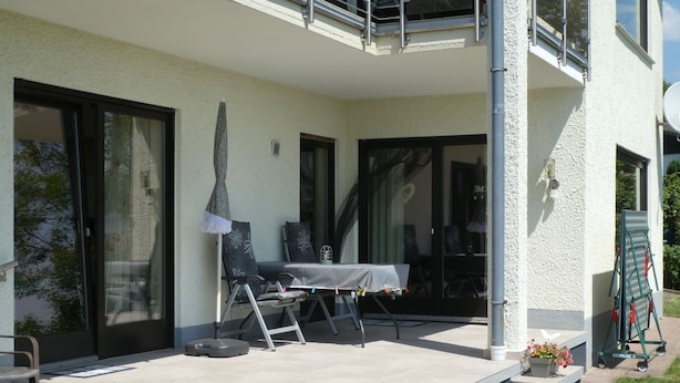A covered outdoor patio with a table and chairs, a small garden area with a planter, and a green folding chair. - Large, bright apartment right next to the forest with a beautiful view (Welschneudorf)