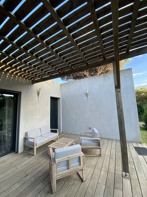 Un patio al aire libre con suelo de madera, una pérgola con luces colgantes y diferentes áreas de estar.