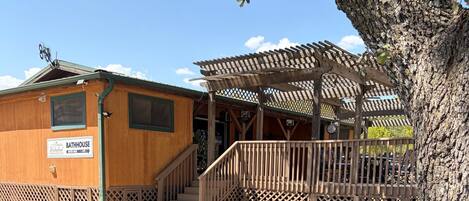 A portable grill and picnic table in a campsite setting with a wooden building labeled 'Bathhouse' in the background.