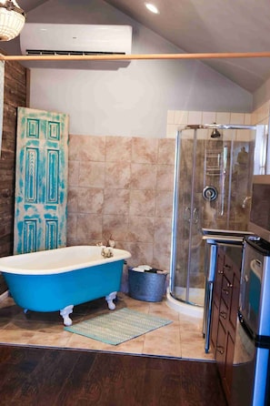 A bathroom with a clawfoot bathtub, a shower enclosure, and a wooden door with a geometric pattern.