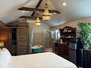 A bedroom with a large bed, a bathtub, a shower, and a wooden ceiling.