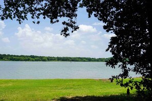 Ein See mit einer grünen Uferwiese und Bäumen, die den Blick einrahmen.
