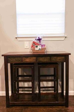 A dark wooden table with drawers and shelves, positioned in front of a window with blinds.