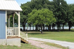 A small building with a porch, a paved path, and a lake in the background. - Lakefront Escape on 14+ Private Acres | Fish, Swim & Relax (Little Elm)