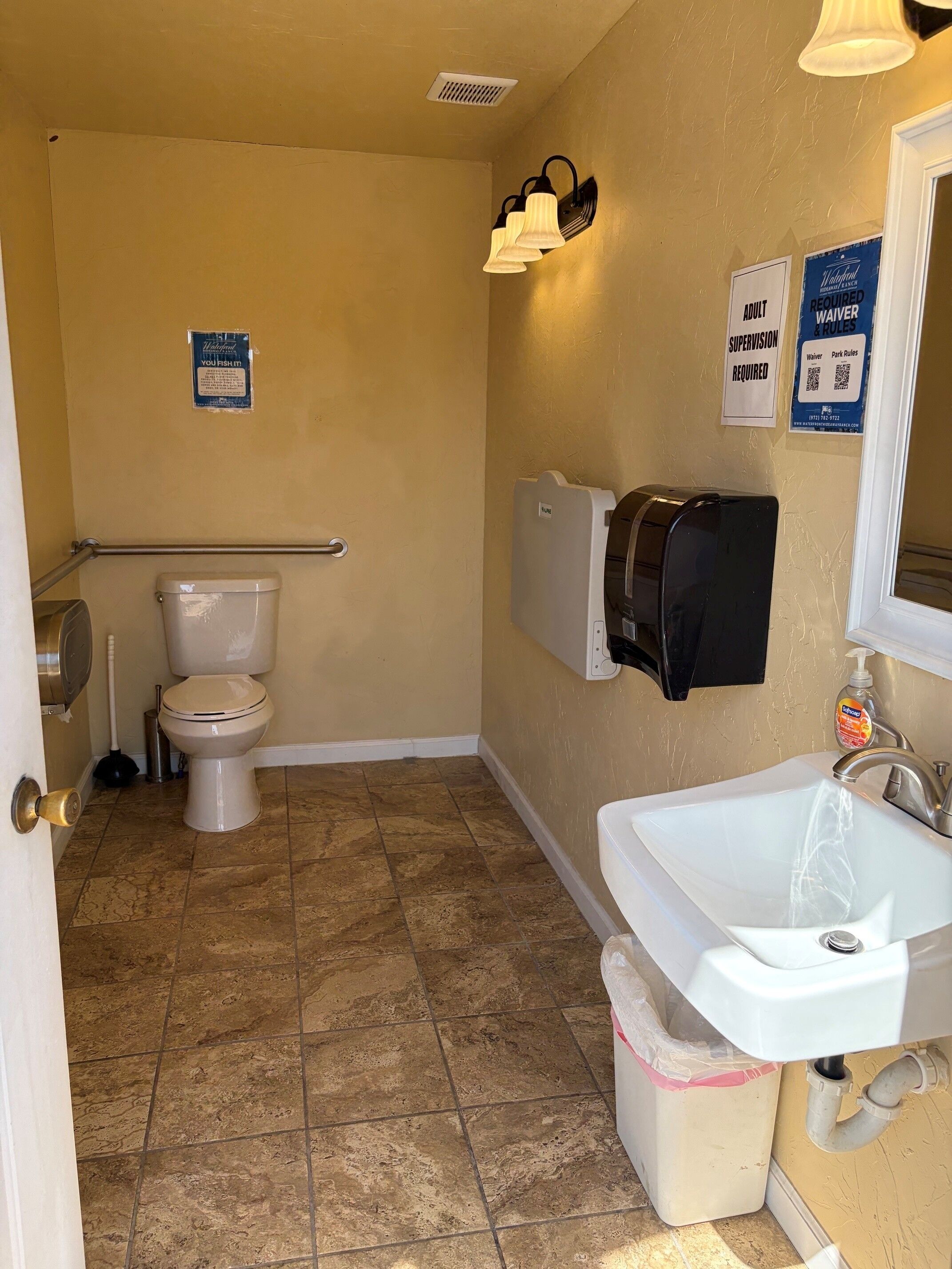 Un bany amb vàter, un lavabo i un dispensador de paper de cuina.