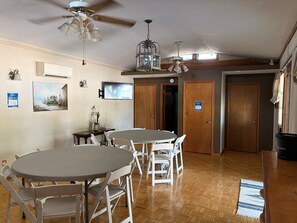 A dining area with two round tables and white chairs, a ceiling fan, and a mounted television.