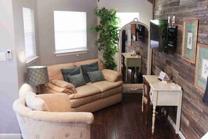 A living room with a beige sofa, a small table, a lamp, a mirror, and a large plant. - Lakefront Escape on 14+ Private Acres | Fish, Swim & Relax (Little Elm)