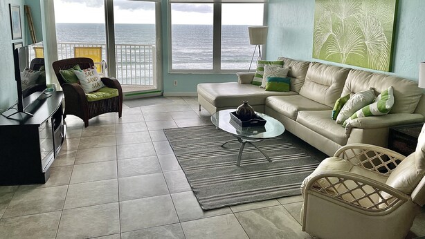 A living room with a view of the ocean, a sofa, a chair, a coffee table, and a TV.