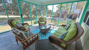 A covered outdoor seating area with wicker furniture, a round table, and a patterned rug.