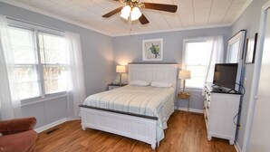 A bedroom with a bed, two bedside tables, a ceiling fan, a television, and a dresser.