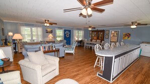 A spacious living room with a large sofa, a dining table, and a kitchen area with white cabinets.