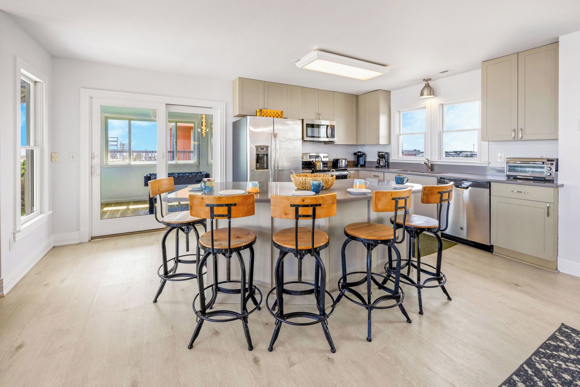 A modern kitchen with a central island, bar stools, and a view of the outdoors.