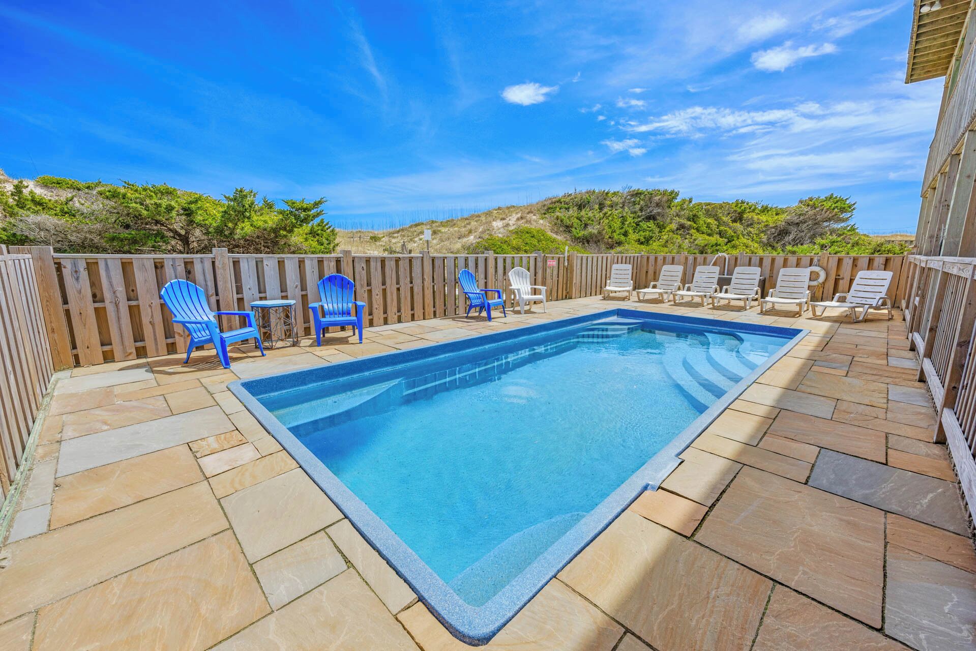 A rectangular swimming pool with a wooden deck surrounding it, featuring a mix of stone and wooden tiles.
