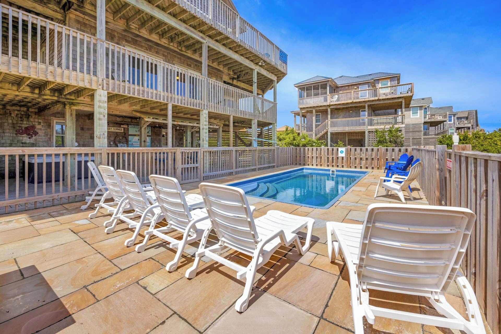 A rooftop pool area with multiple levels of balconies, white lounge chairs, and a clear blue sky.