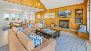 A spacious living room with a wooden ceiling, a fireplace, and a dining area with a view of the outdoors.