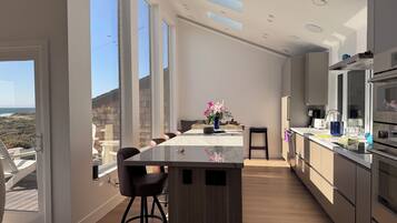 A modern kitchen with a large island, bar stools, and a view of the beach.