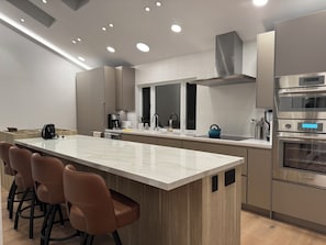 Une cuisine moderne dotĂ©e dâun Ăźlot central, dâappareils Ă©lectromĂ©nagers en acier inoxydable et dâun coin repas avec des tabourets de bar.