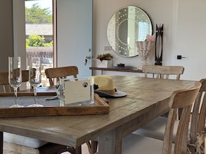 Une table Ă manger en bois, avec des chaises, un miroir et un plateau sur lequel se trouvent une carte et des verres.
